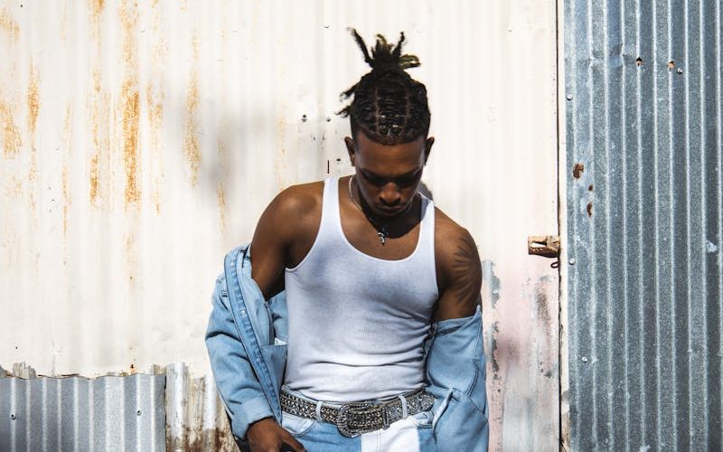 Stylish young man in trendy denim attire against a rustic metal background.
