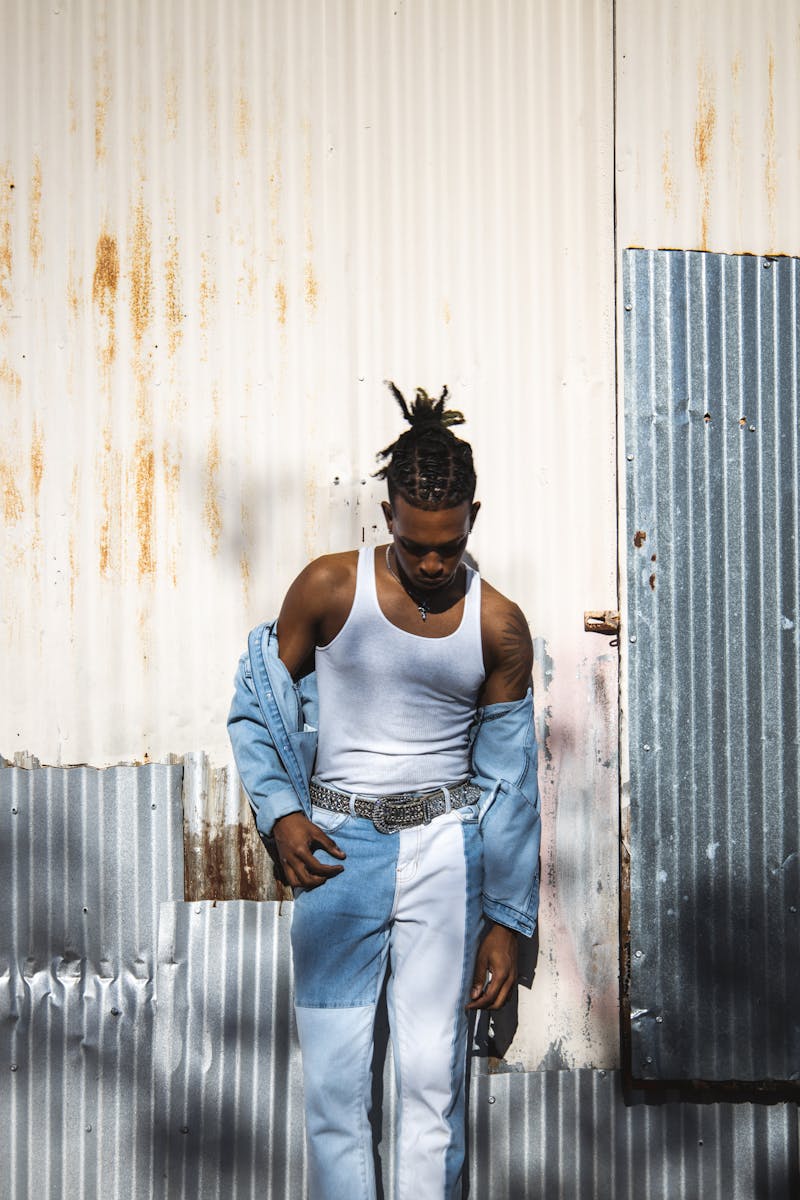 Stylish young man in trendy denim attire against a rustic metal background.