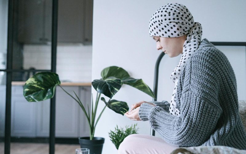 Woman in headscarf sitting indoors, taking medication, symbolizing cancer care and support.