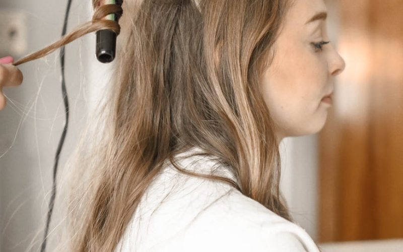 Profile of a woman having her hair curled with an iron in a salon setting.